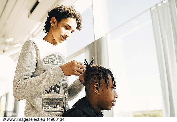 Teenage boy styling friend's hair while standing in restaurant