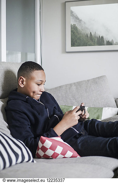 Teenage boy using mobile phone on sofa in living room