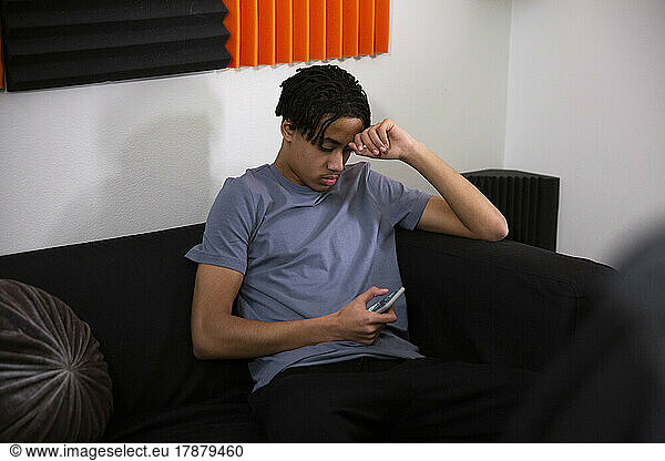 Teenage boy using smart phone while sitting on sofa in recording studio