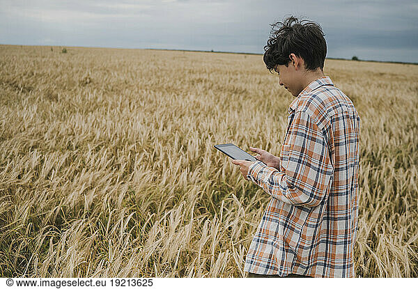 Teenage boy using tablet PC in wheat field
