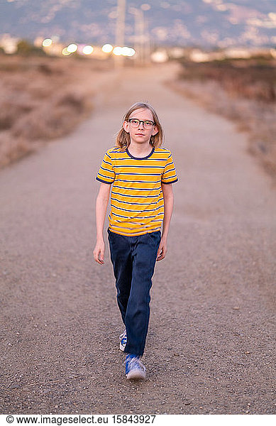 Teenage boy walking along dirt road at sunset