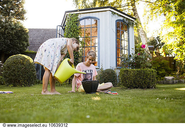 Teenage boy watching sister watering potted plant in backyard