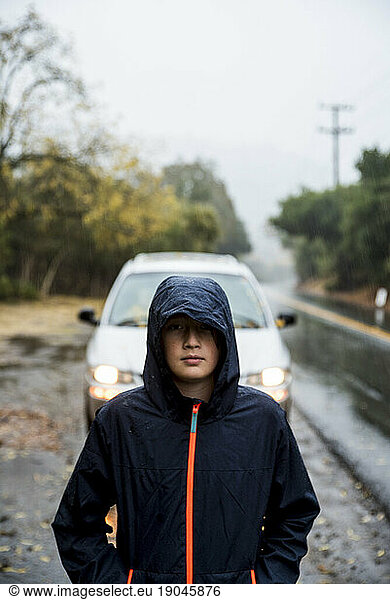 Teenage boy wearing rain jacket standing in front of minivan