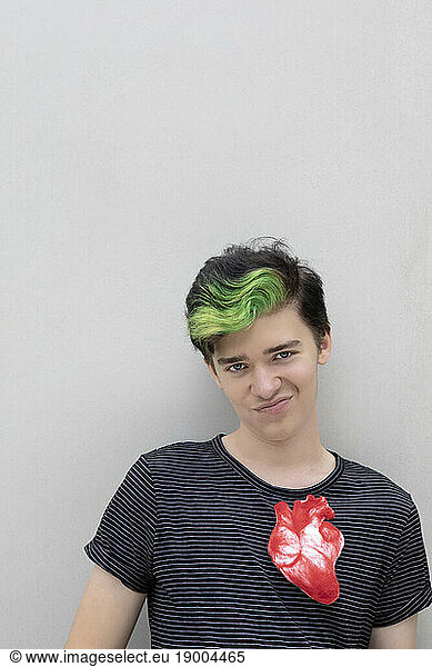 Teenage boy with dyed green hair and artificial heart against gray background