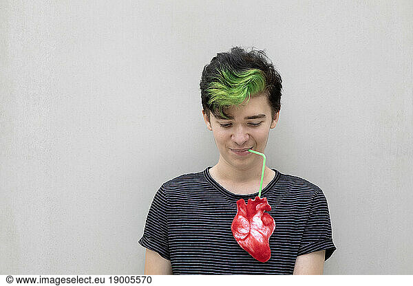 Teenage boy with dyed green hair drinking from heart against gray background