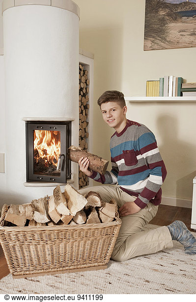 Teenage boy with log in front of fireside