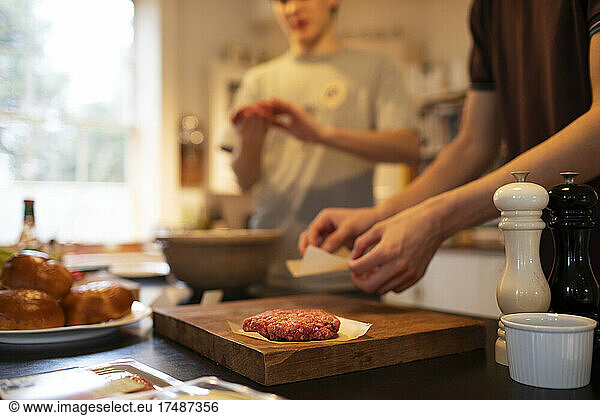 Teenage boys making hamburger patties in kitchen
