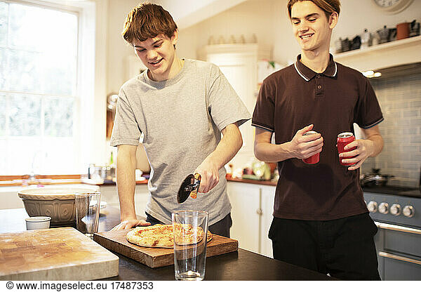 Teenage boys slicing pizza in kitchen