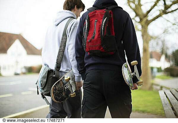 Teenage boys with skateboards walking on sidewalk