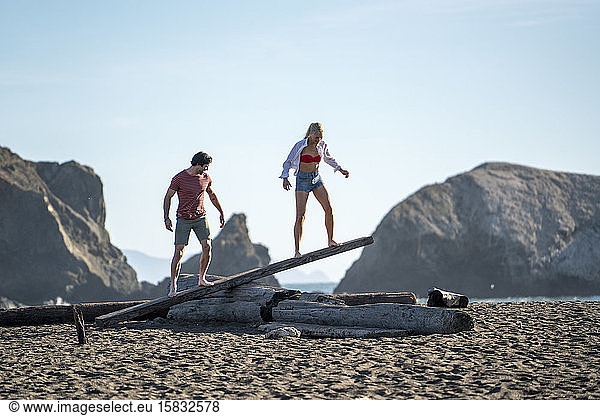 Teenage couple balancing on driftwood see-saw on beach