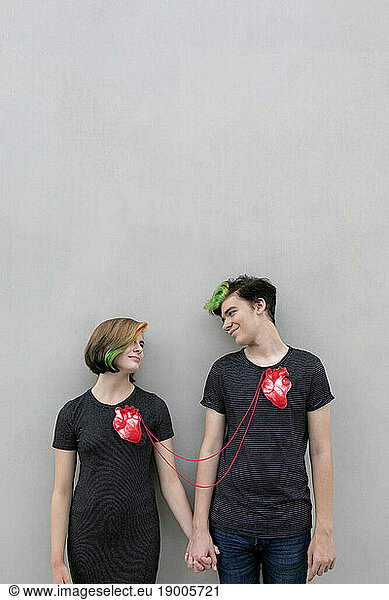 Teenage couple connected with hearts against gray background