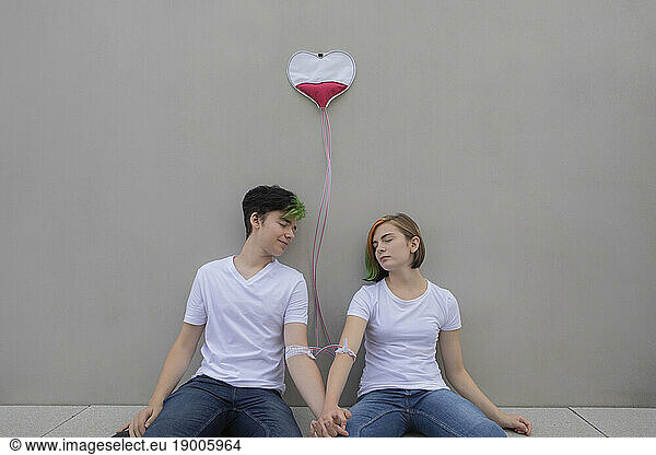 Teenage couple connected with IV drips relaxing in front of gray wall