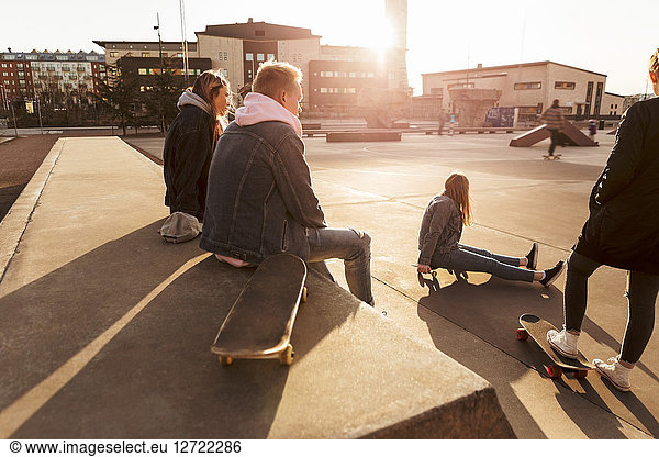 Teenage friends hanging out at skateboard park during sunny day