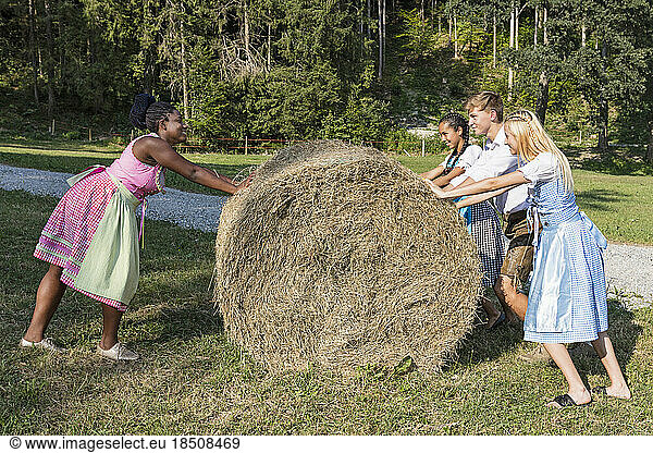 Teenage friends pushing straw bale  Bavaria  Germany
