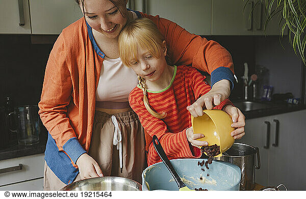 Teenage girl and her younger sister putting raisins in mixing bowl at kitchen