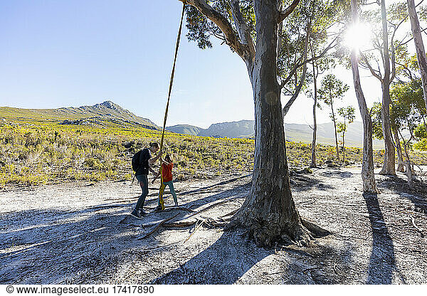 Teenage girl and younger brother using rope swing on a hiking trail