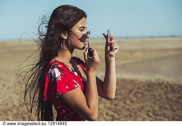Teenage girl applying lip gloss on the beach