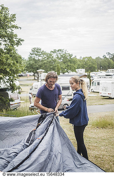 Teenage girl assisting father in pitching tent at campsite