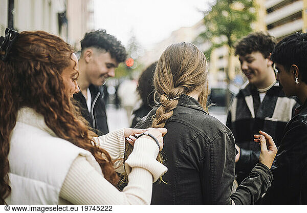 Teenage girl braiding hair of female friend standing at street