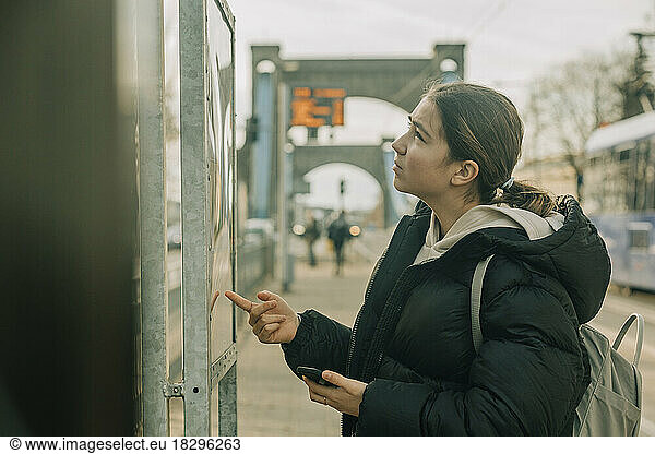 Teenage girl checking arrival departure board at tramway station