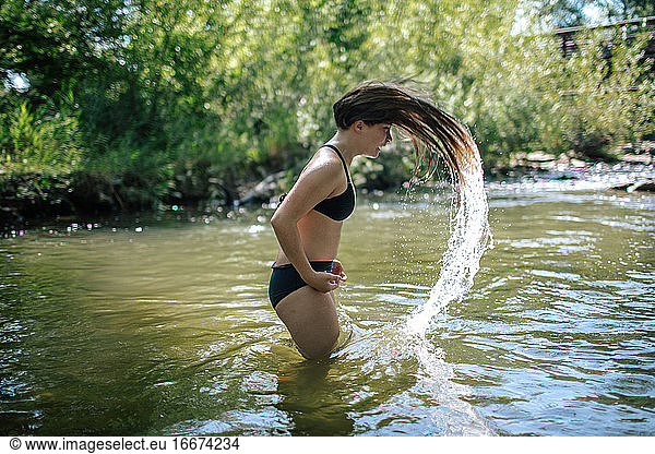 Teenage girl flipping wet hair in a creek on a summer day