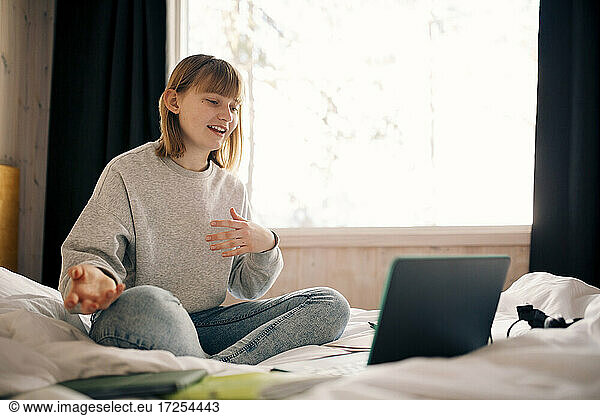Teenage girl gesturing while attending video call during homeschooling in bedroom