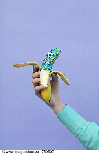 Teenage girl holding banana by lavender background