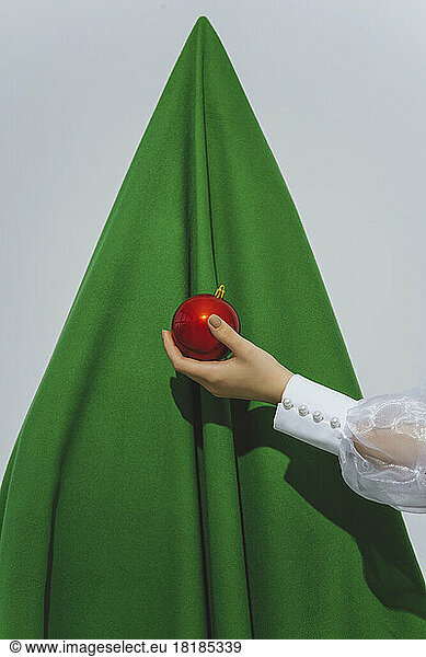 Teenage girl holding red ornament in front of abstract Christmas tree