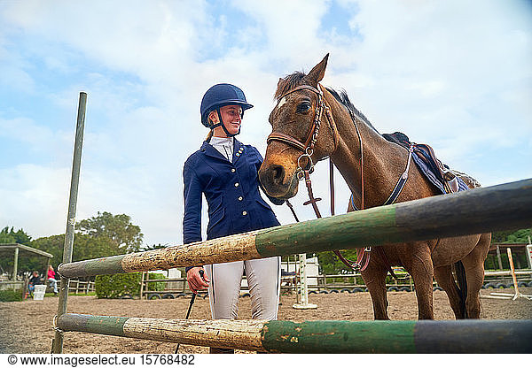 Teenage girl in equestrian helmet with horse at obstacle in paddock