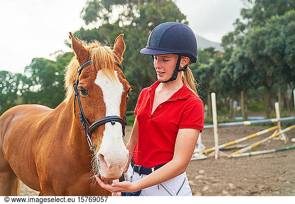 Teenage girl in equestrian helmet with horse in paddock