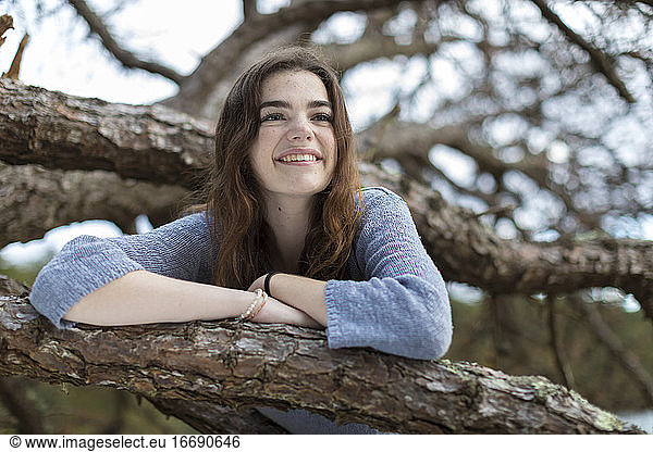 Teenage girl in tree branches  smiling with freckles and long hair