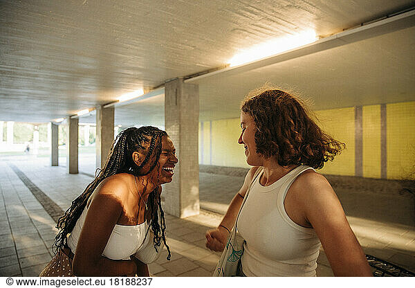 Teenage girl laughing by female friend while enjoying under bridge