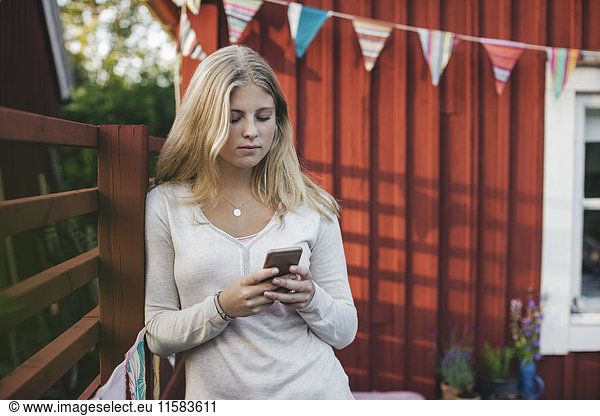 Teenage girl leaning on fence while text messaging against house in back yard