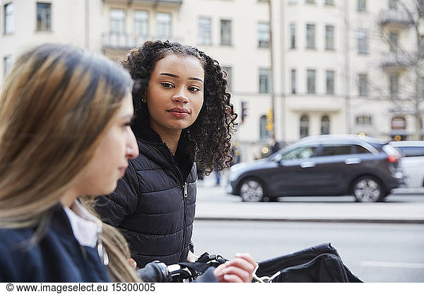 Teenage girl looking at female friend by street in city