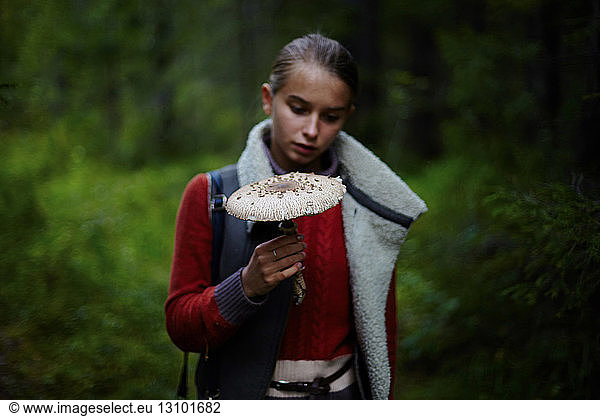 Teenage girl looking at large mushroom while standing in forest