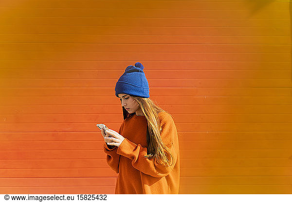 Teenage girl looking at smartphone in front of orange background