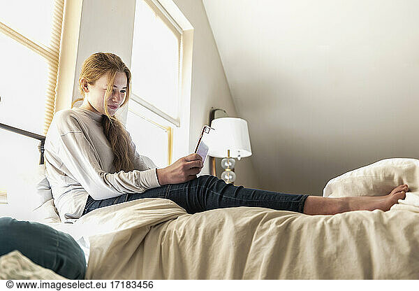 teenage girl lying in bed using her smart phone