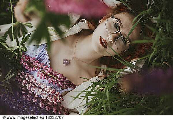 Teenage girl lying on grass with lupin flowers