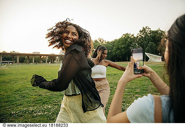 Teenage girl photographing happy female friends dancing in park