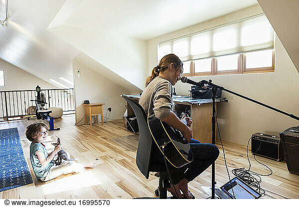 Teenage girl playing her guitar and singing  her brother playing in the background