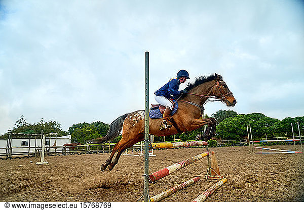 Teenage girl practicing equestrian jumping in paddock