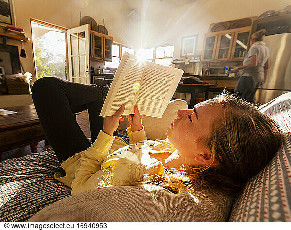 teenage girl reading book at home in early morning light