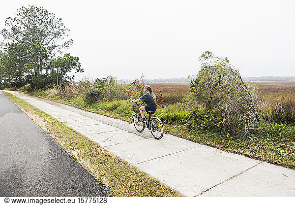 Teenage girl riding a bicycle along a path on open ground by water