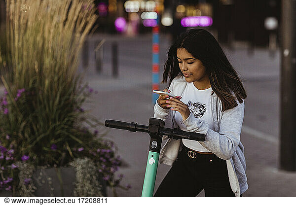 Teenage girl scanning QR code on electric push scooter handlebar with smart phone