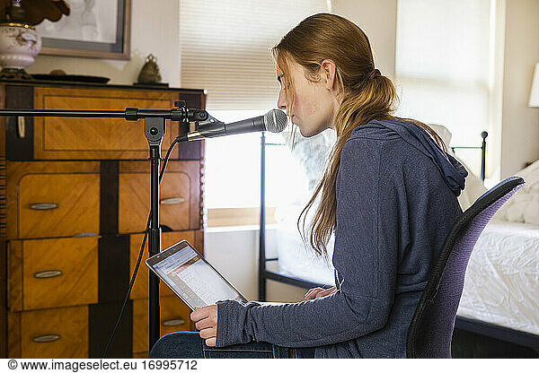 Teenage girl singing into a microphone in her bedroom