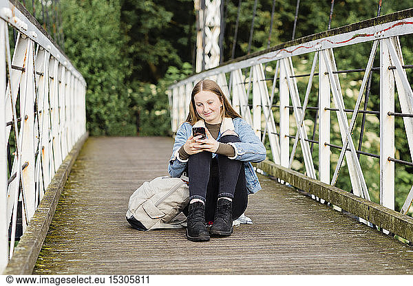 Teenage girl sitting on a bridge and using smartphone