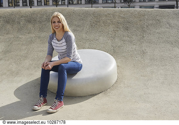 Teenage girl sitting on a round stone in playground  Munich  Bavaria  Germany