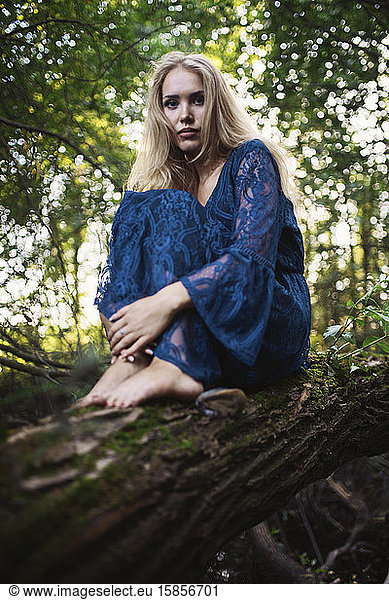 Teenage girl sitting on fallen tree trunk at forest