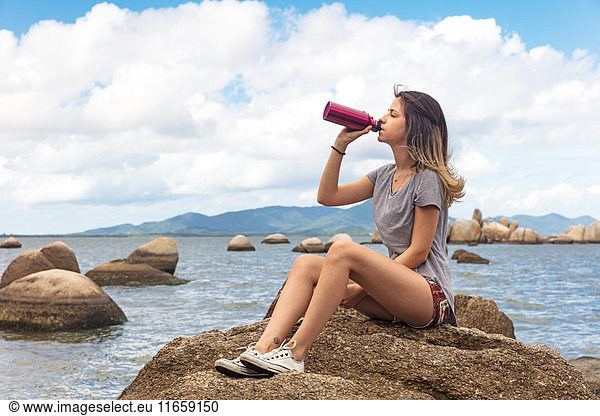 Teenage girl sitting on rocks drinking from water bottle