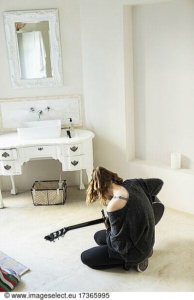 Teenage girl sitting on the floor playing a guitar